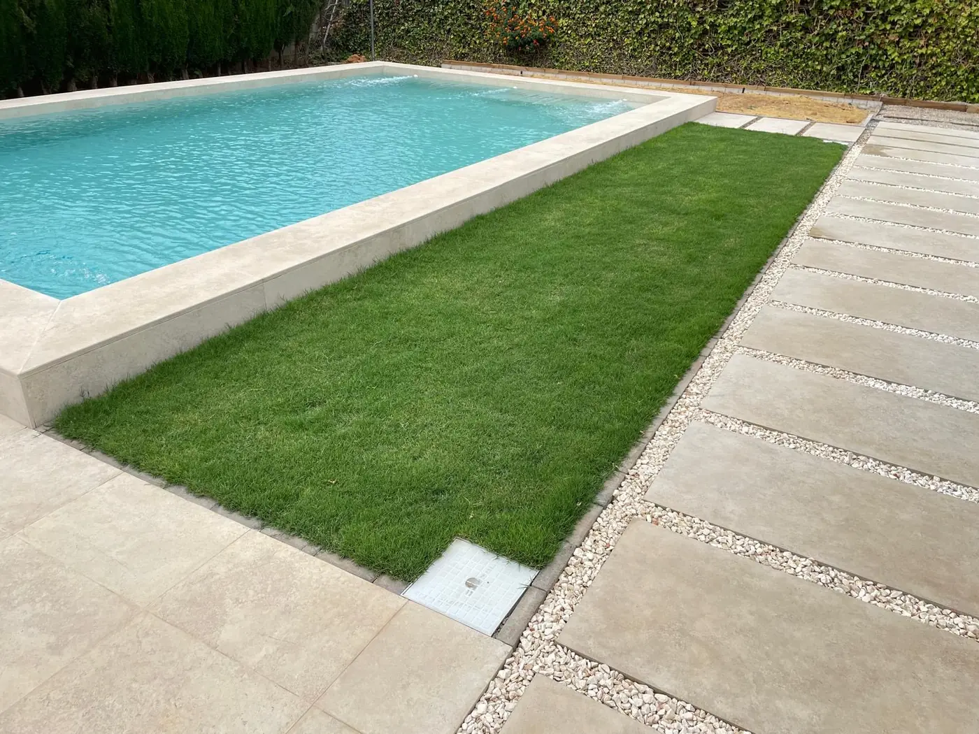 Franja de césped natural junto a una piscina con losas sobre grava blanca, obra en Sevilla